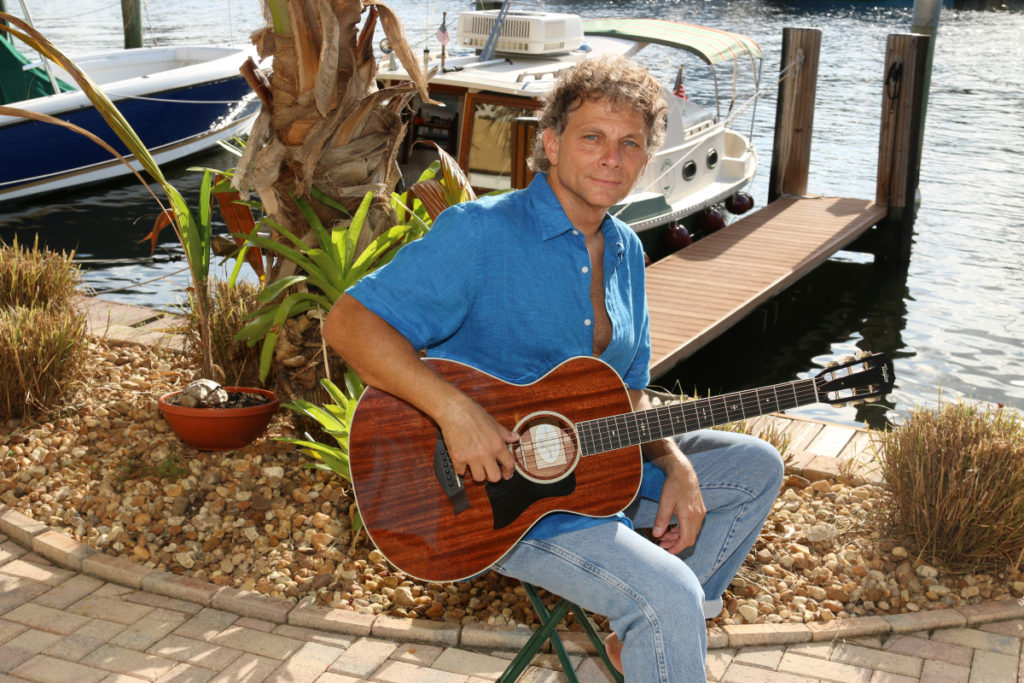 Jimmy Stowe with his acoustic guitar sitting by the dock